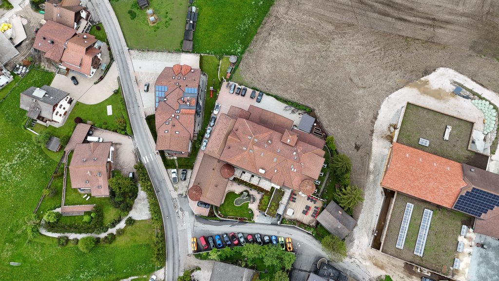 Luftaufnahme des Almhof Hotel Call mit geparkten Mustangs. Zu sehen ist der Parkplatz, das Gebäude und der Whirlpool außen