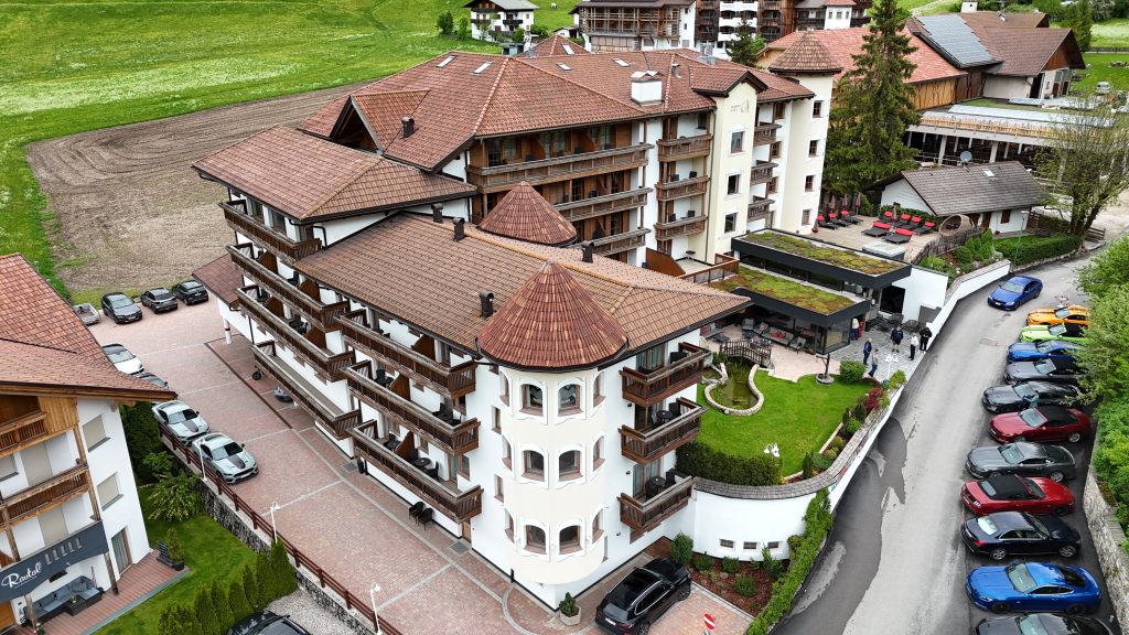 Seitenansicht des Almhof Hotel Call mit davor geparkten Ford Mustangs. Das Hotel hat vier Etagen.