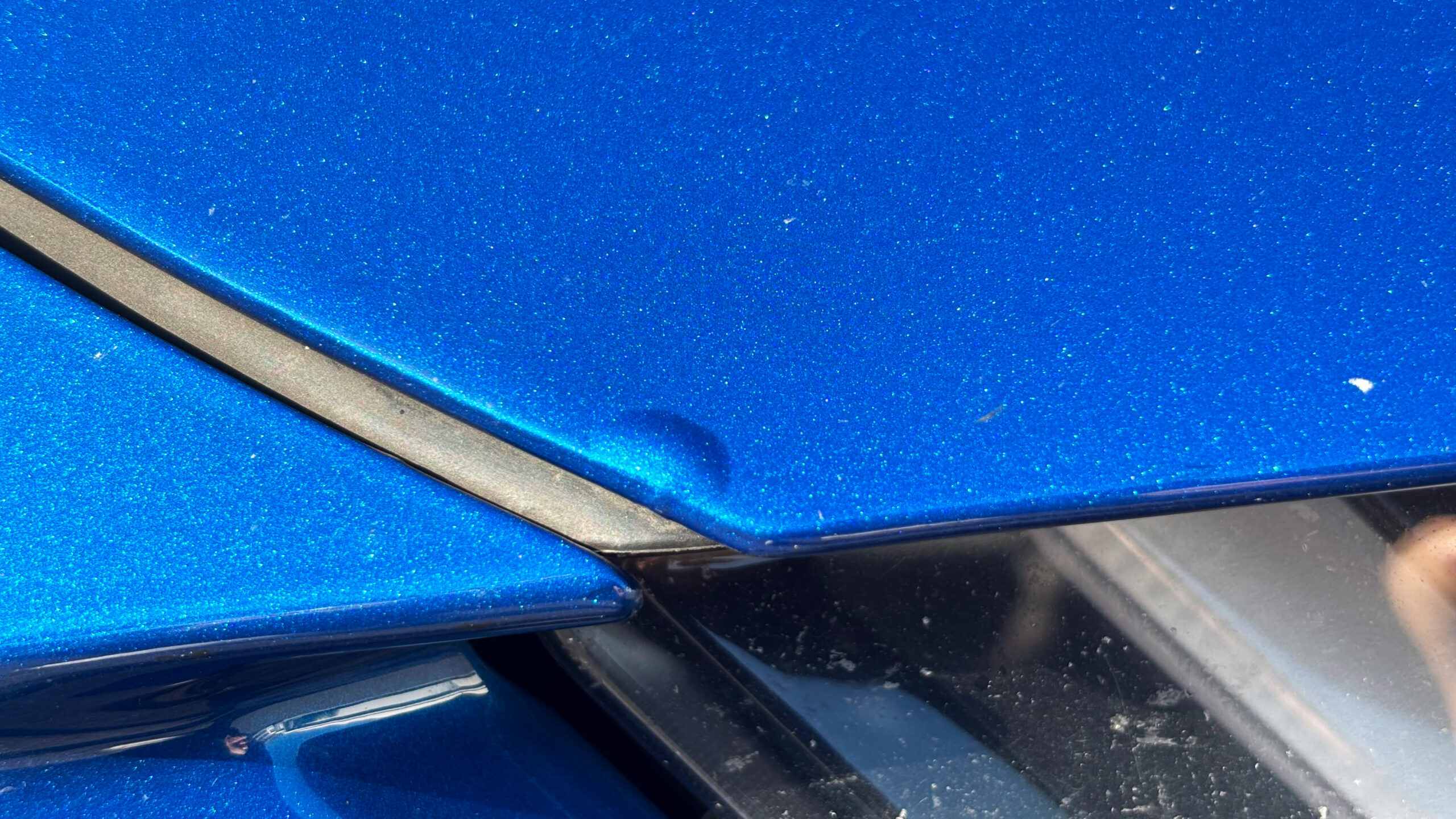 Nahaufnahme eines kleinen Korrosions-Schadens im blauen Lack neben einer Spaltkante.