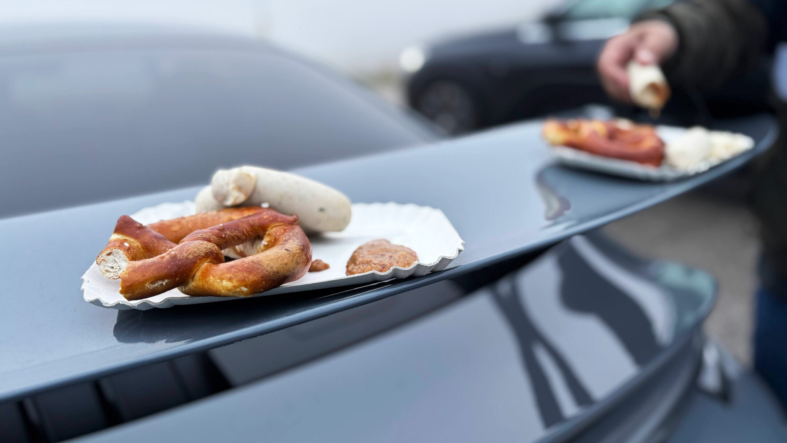 Weißwurst und Brezel auf dem Heckspoiler eines Porsche GT3 bei einem Frühstück.