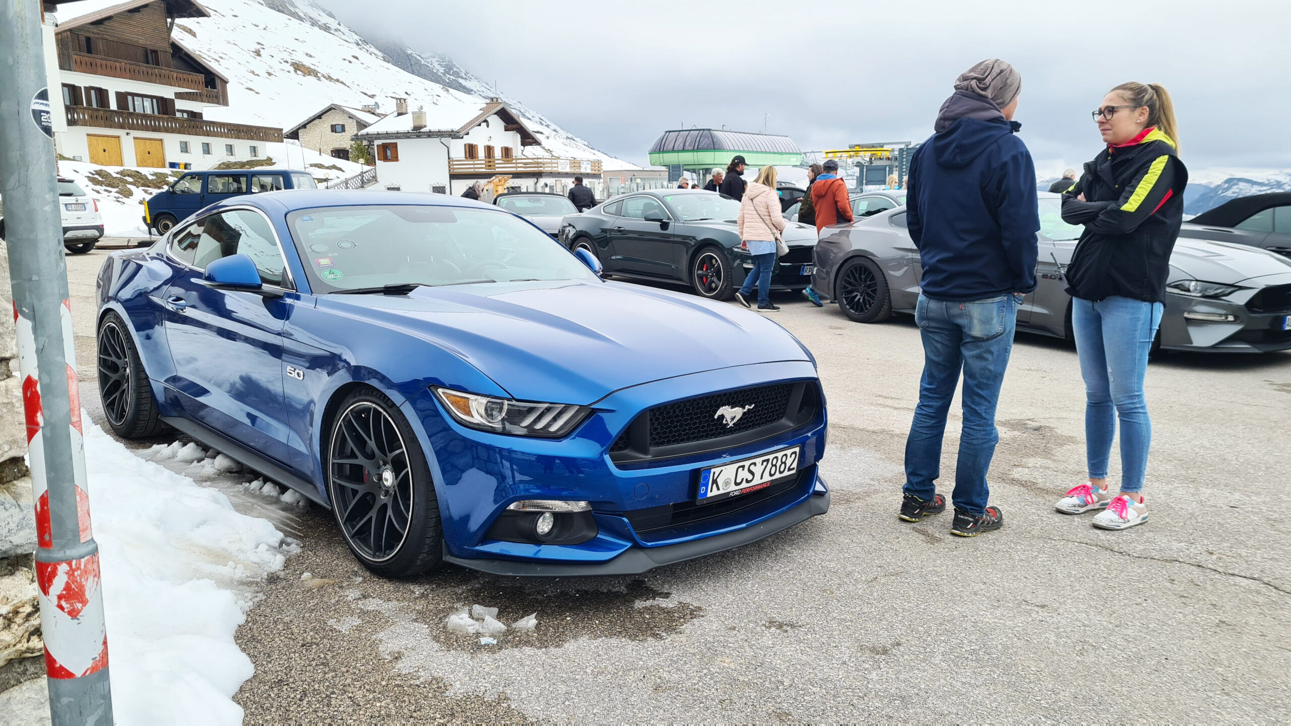 Blauer Mustang umgeben von Menschen in Winterkleidung.