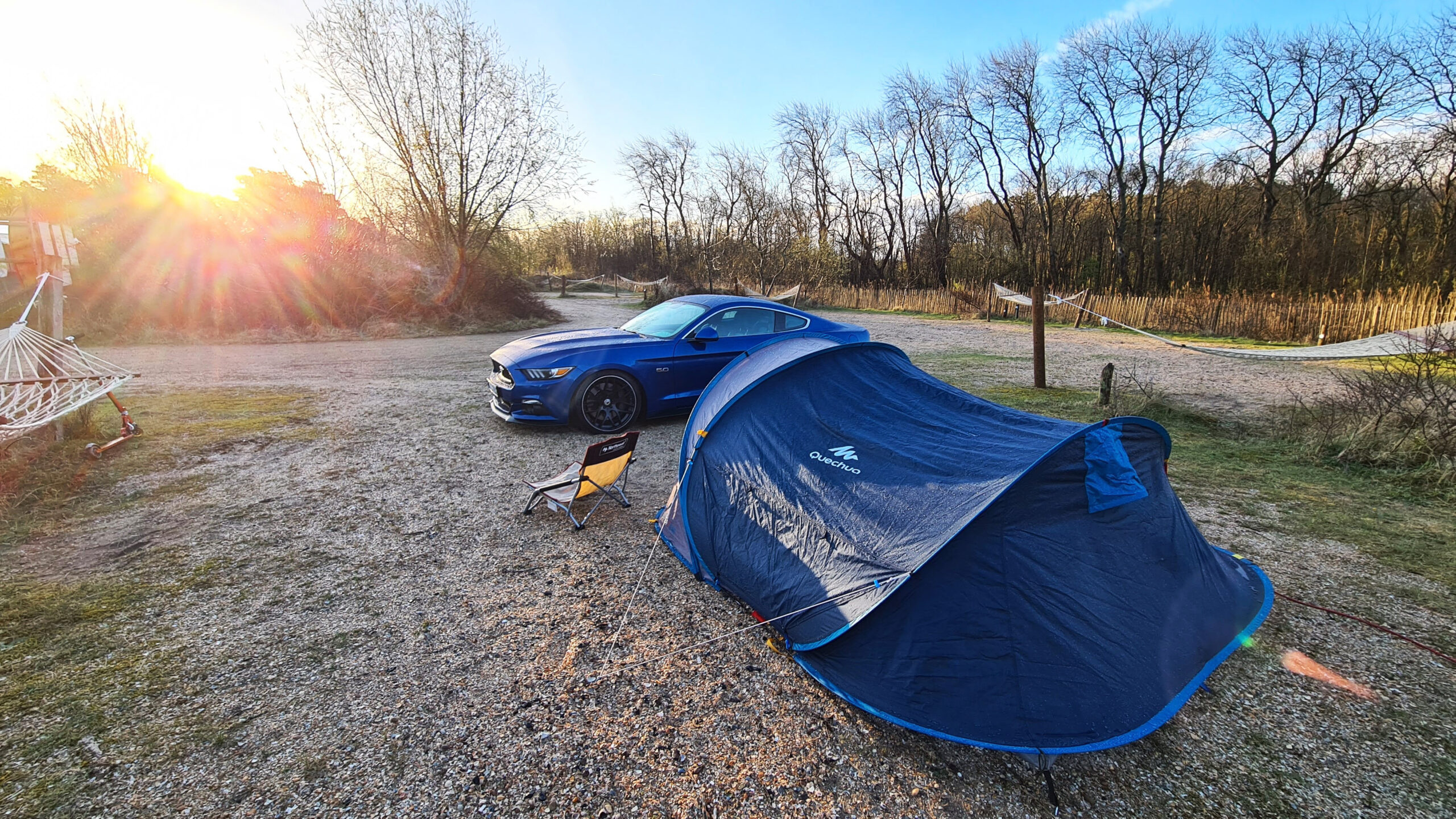 Blauer Mustang neben einem halb aufgebauten Zelt bei Sonnenuntergang.