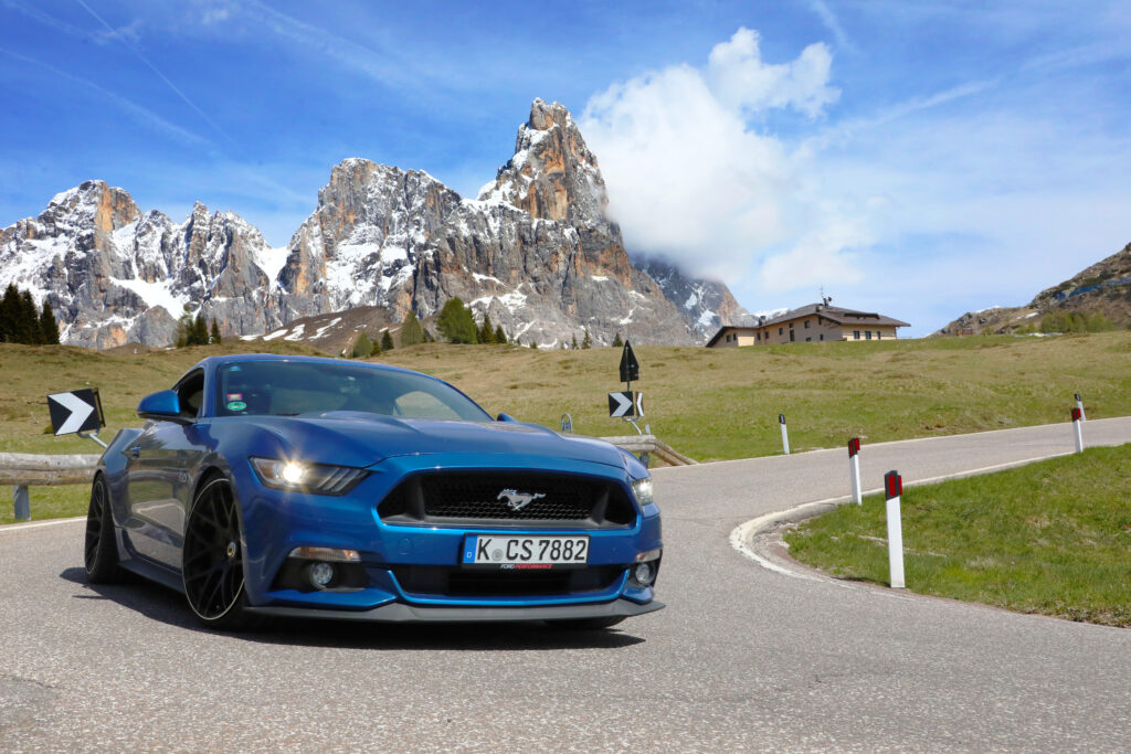 Blauer Mustang vor dramatischer Dolomitenkulisse auf Bergstraße.