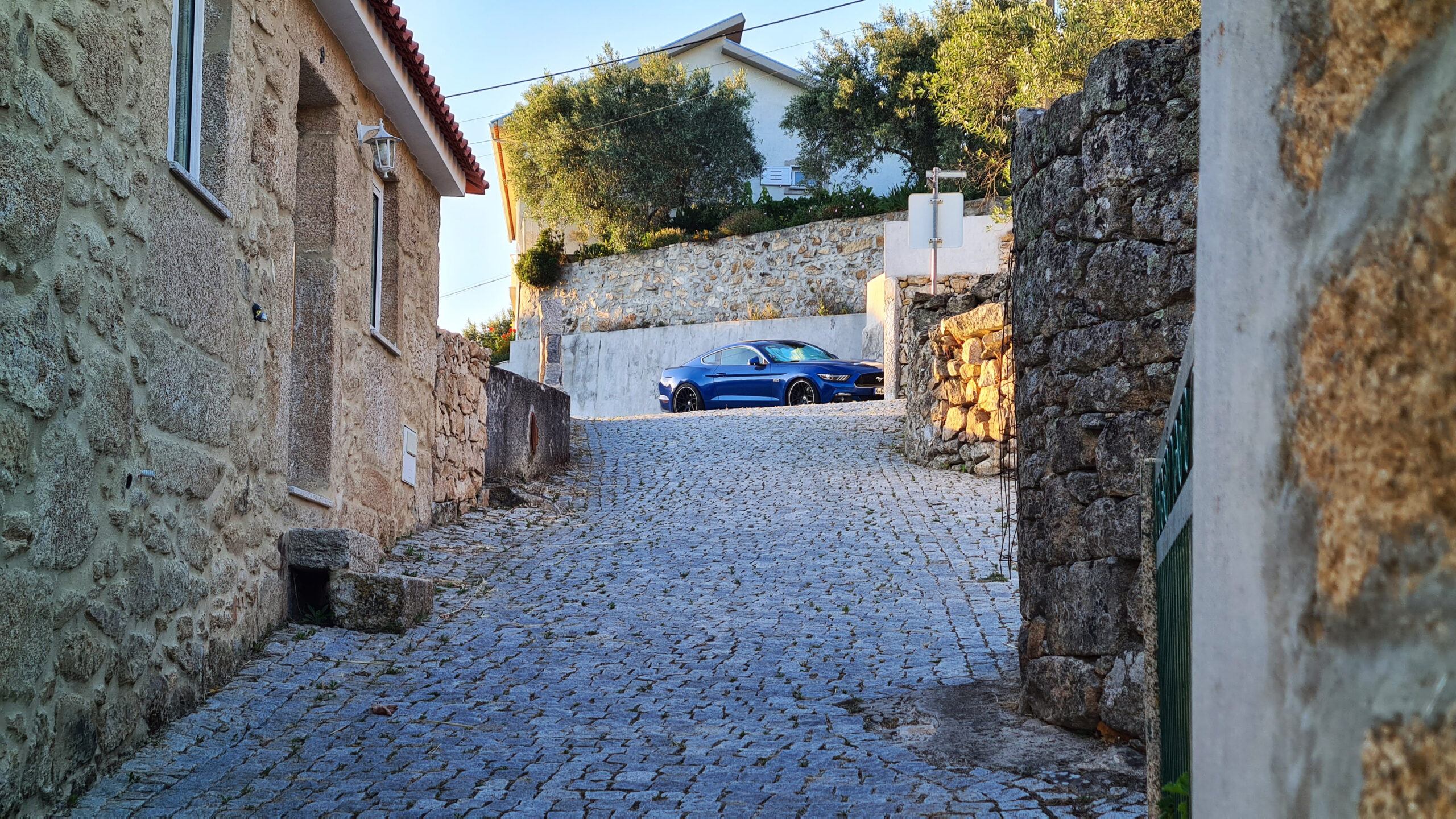 Blauer Mustang steht an einer engen, gepflasterten Gasse mit Steinmauern.