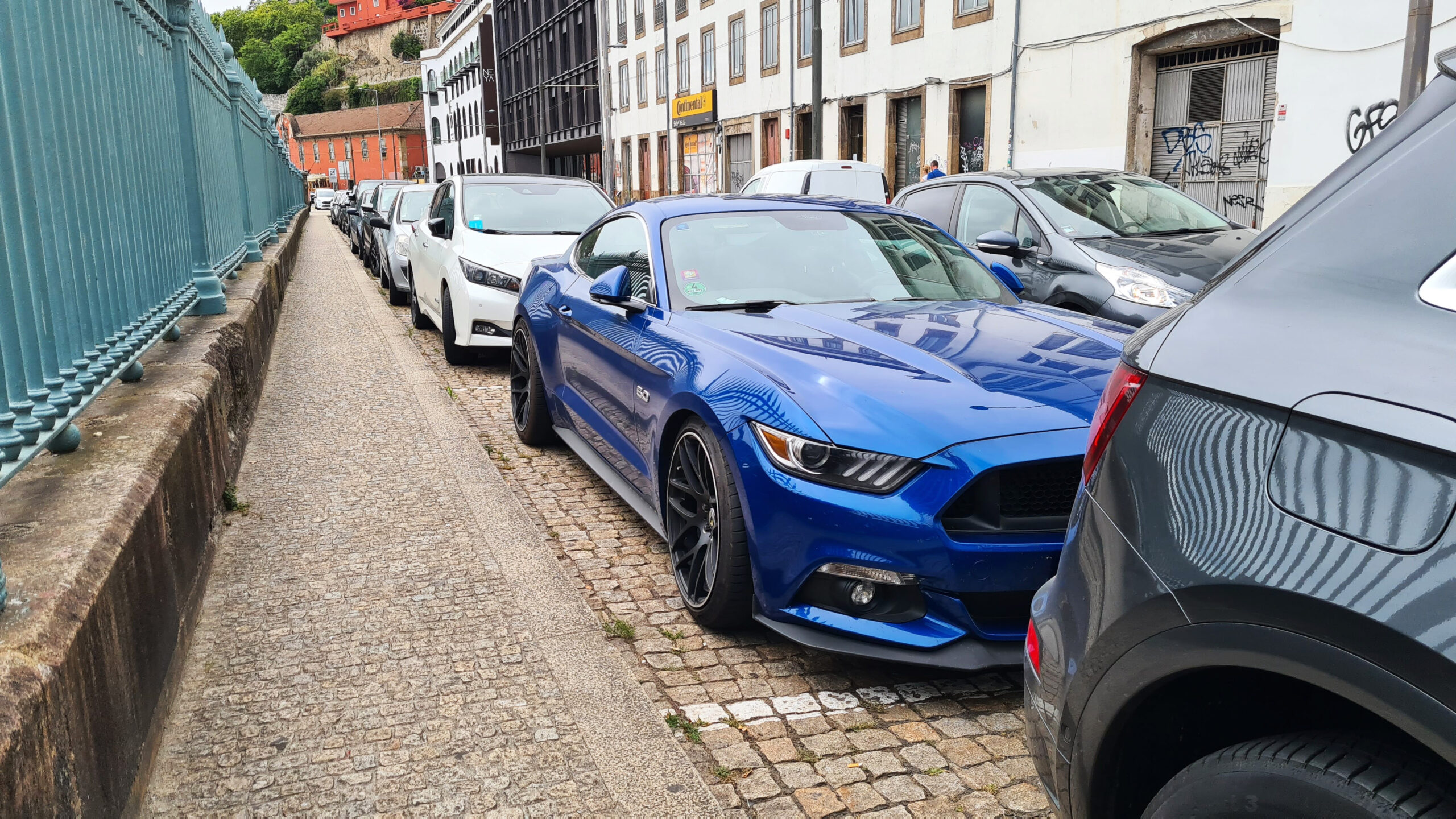 Blauer Mustang ist in Porto in eine enge Parklücke zwischen Bordstein und Auto gequetscht.