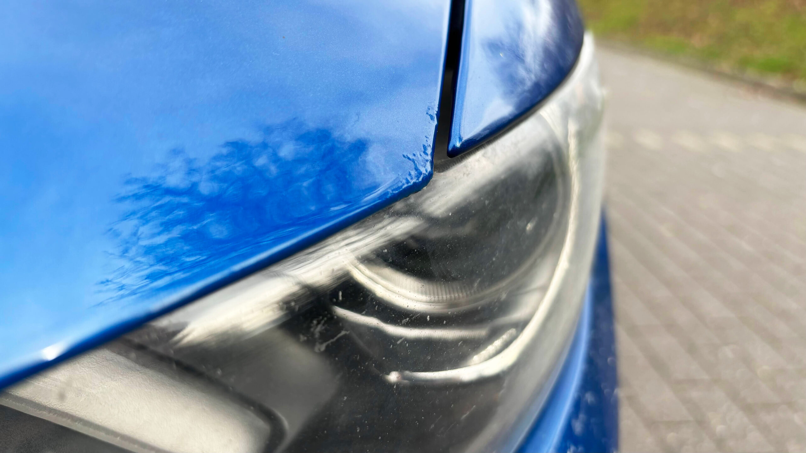 Nahaufnahme der auftretenden Korrosion an der Motorhaube eines blauen Mustangs.