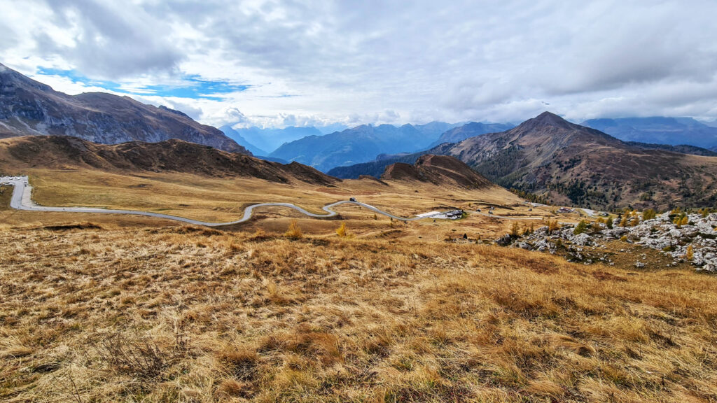 Weite Straße durch herbstliche Hügellandschaft in den Dolomiten am Passo Giau.