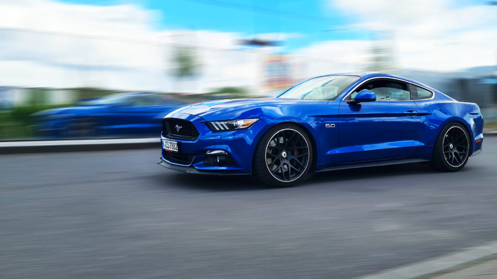 Ein saphirblauer Ford Mustang fährt mit hoher Geschwindigkeit an der Kamera vorbei